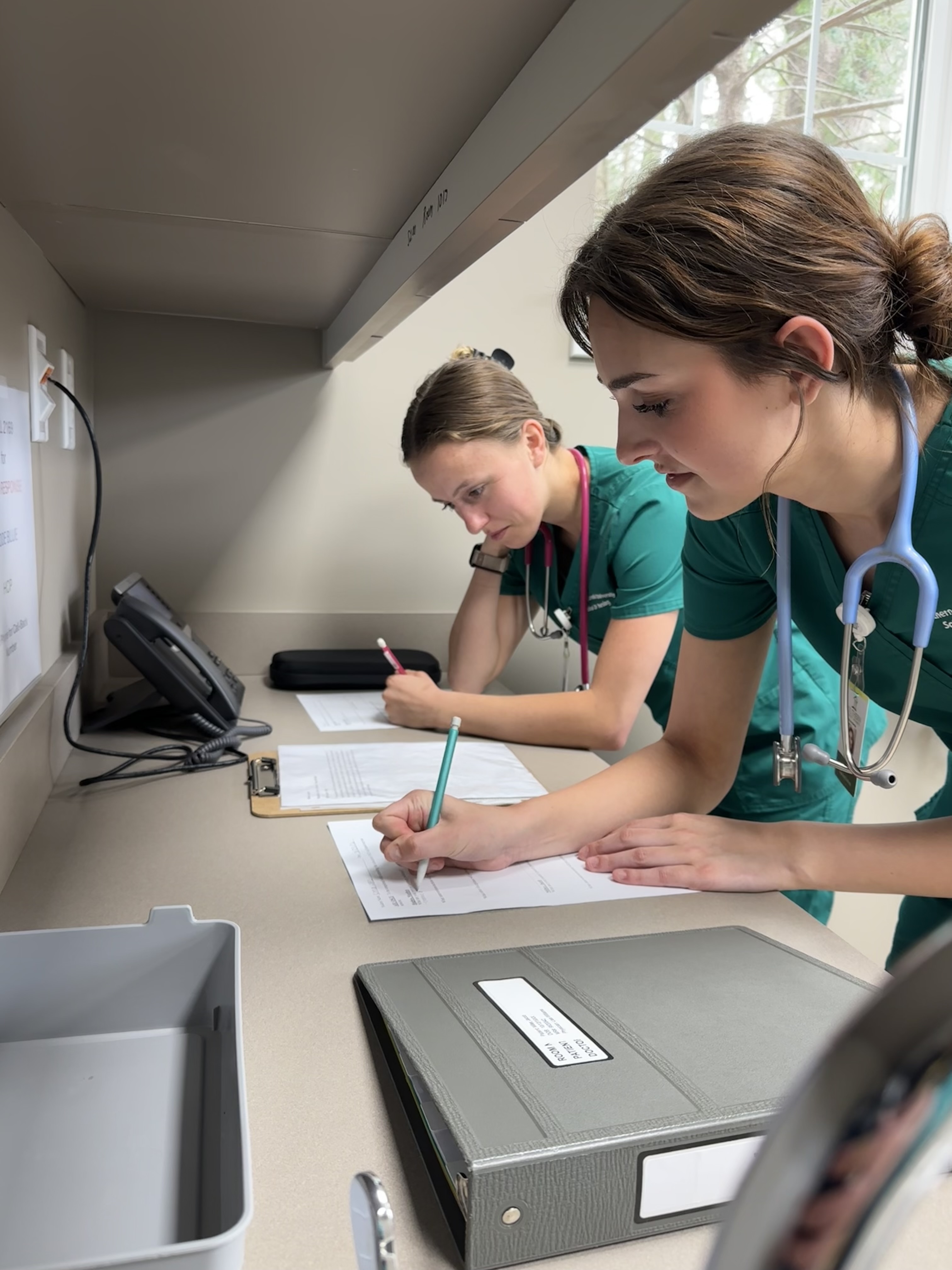 Two female students complete notes during sim lab.