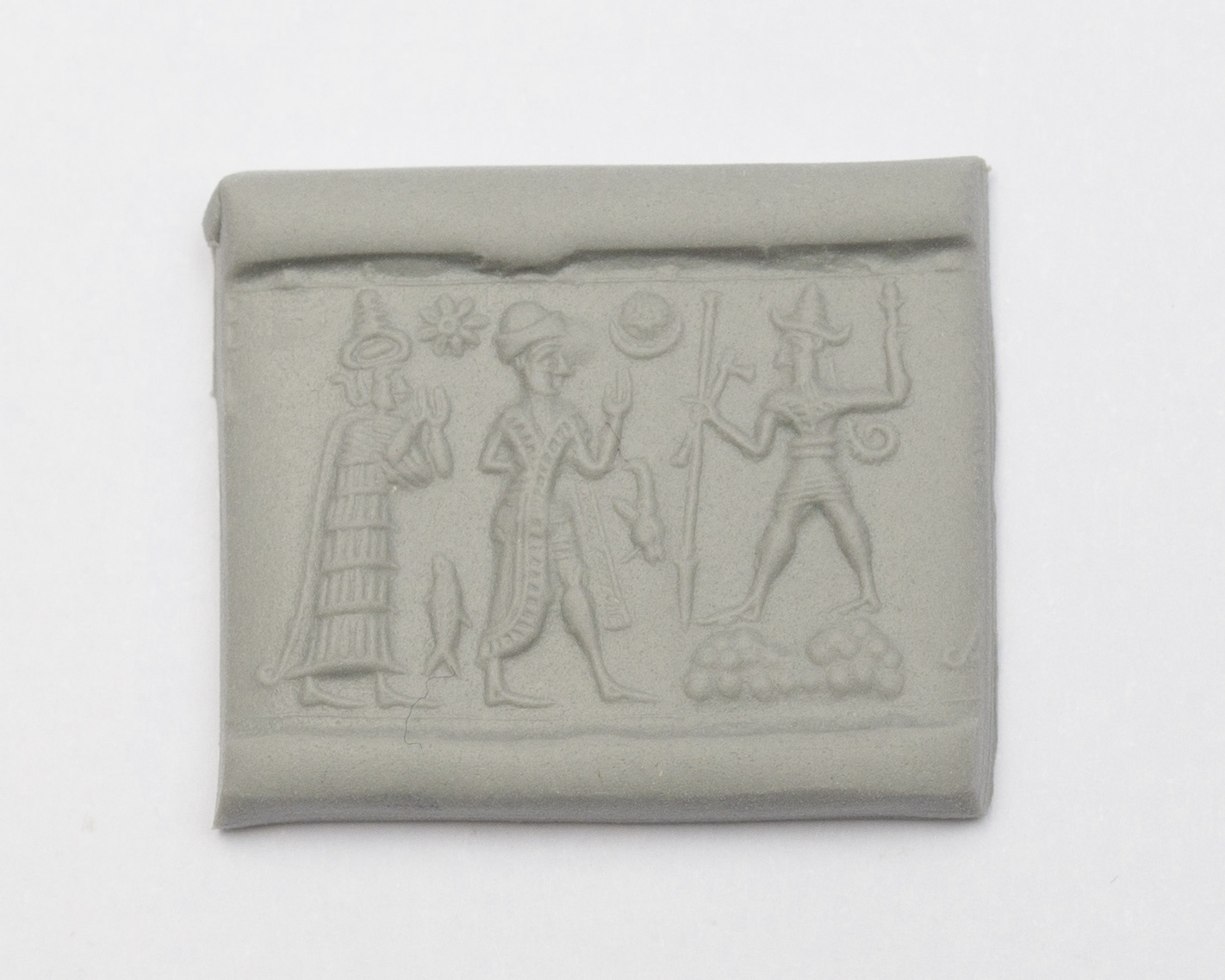 a seal impression set in a piece of clay, featuring three elaborately dressed figures