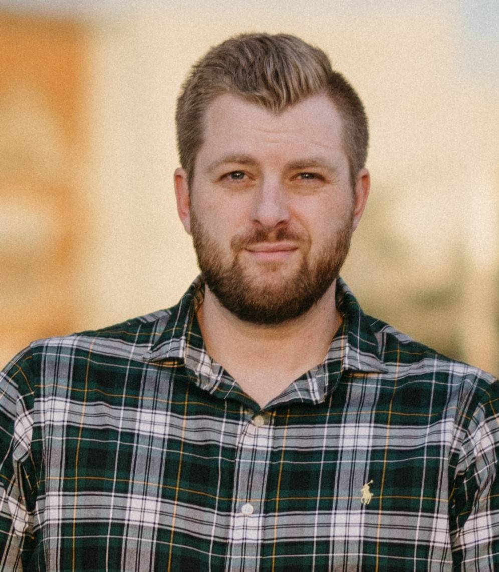 Headshot of Brandon wearing a striped polo in an outdoor professional setting. 