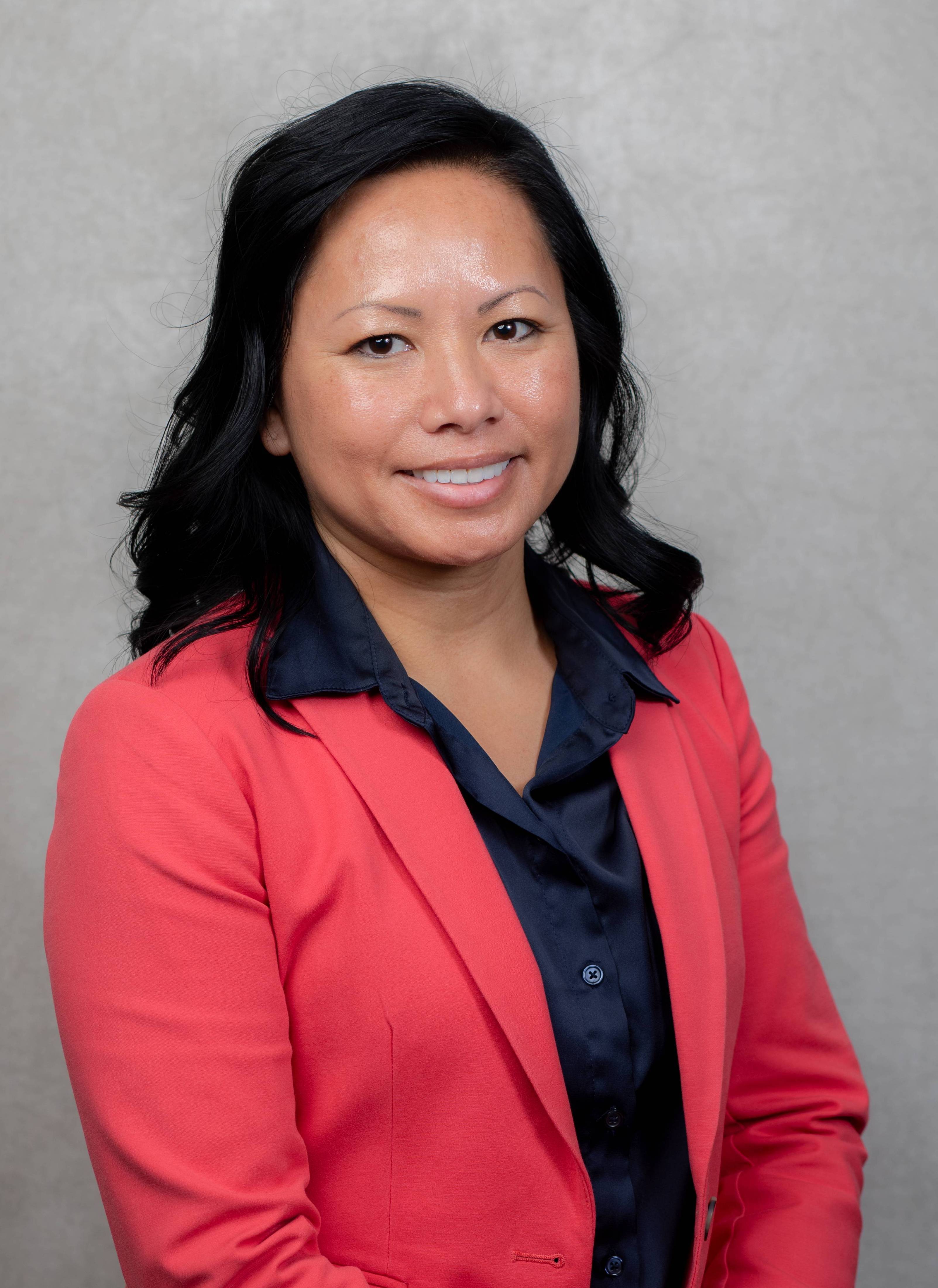 An professional portrait of Loni wearing a coral suit with a light grey background.