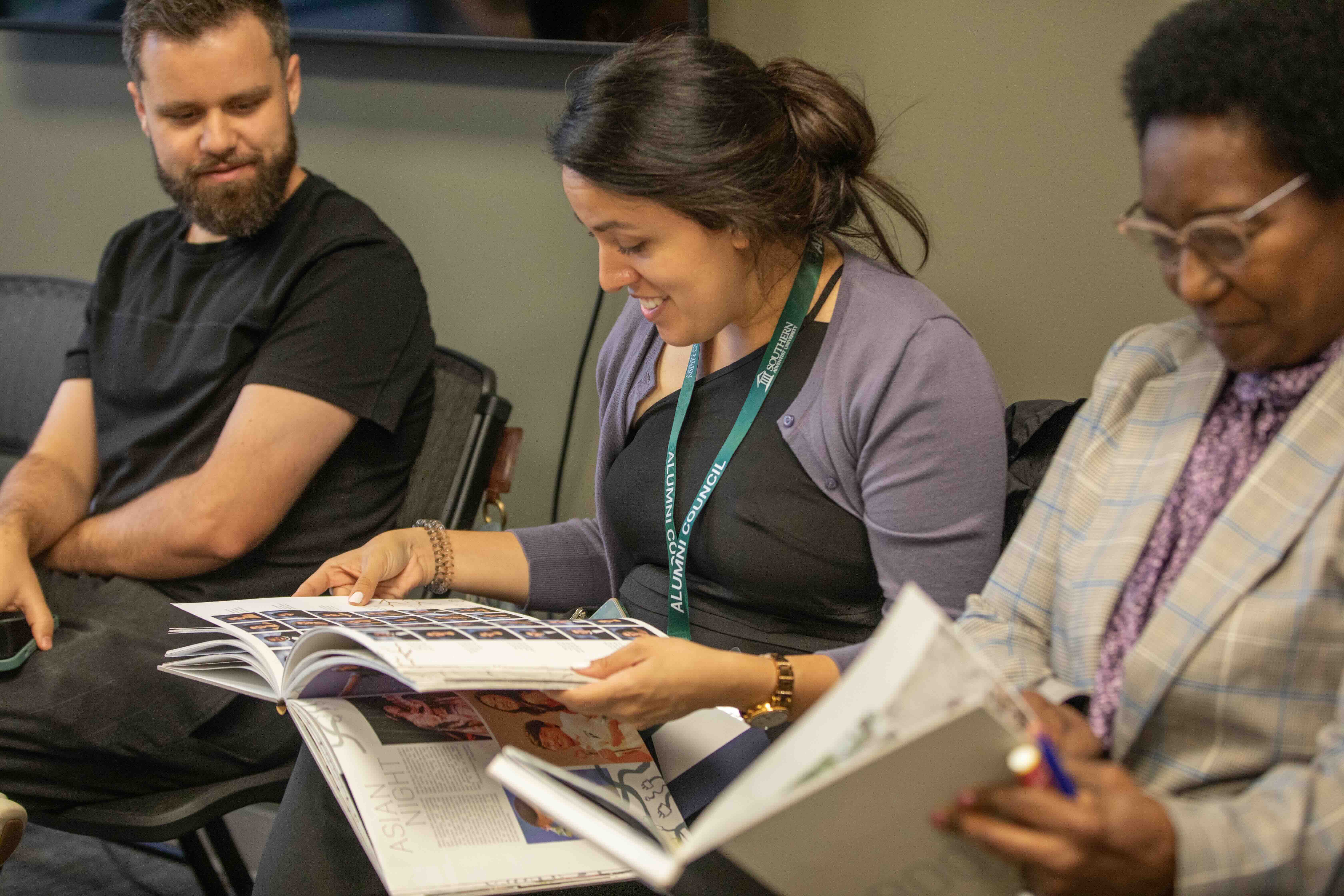 3 alumni sitting together looking through yearbooks