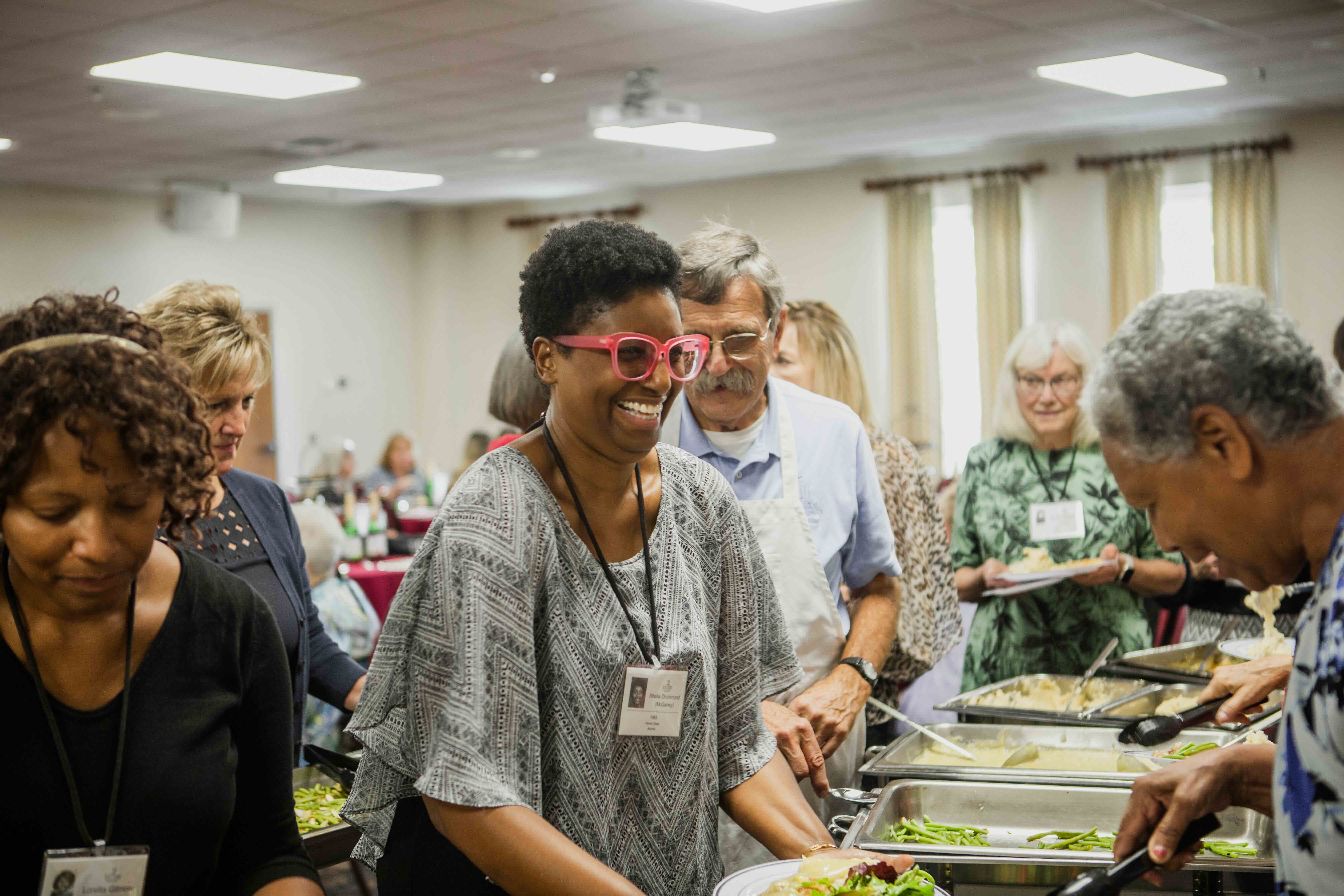 A woman laughing while standing in a buffet food line.