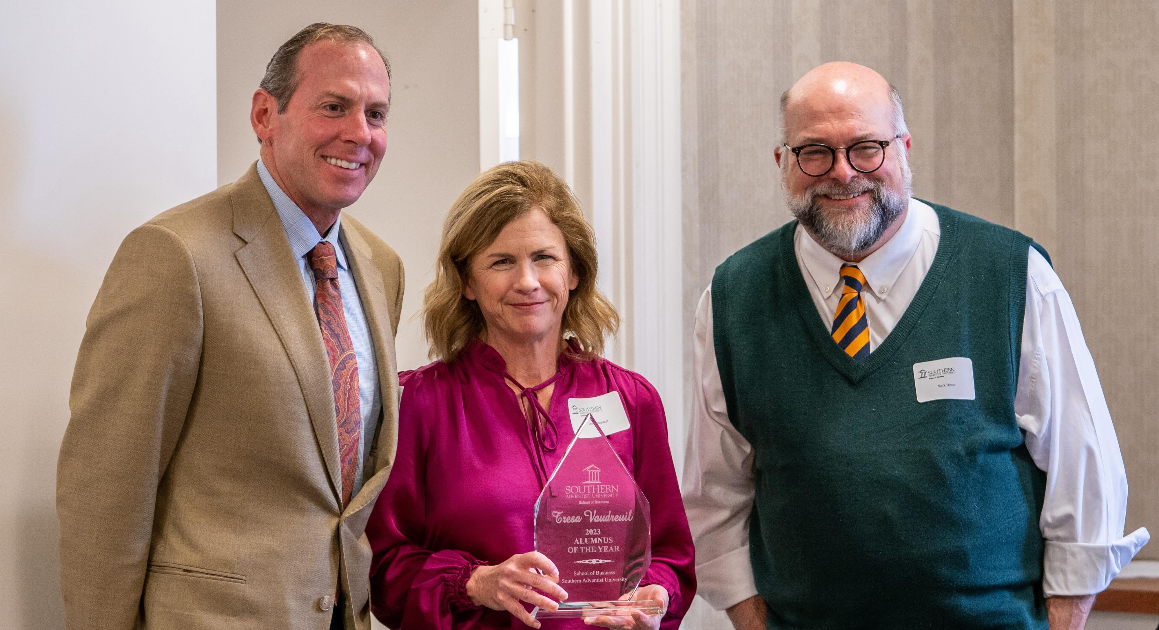 three people smiling with an award
