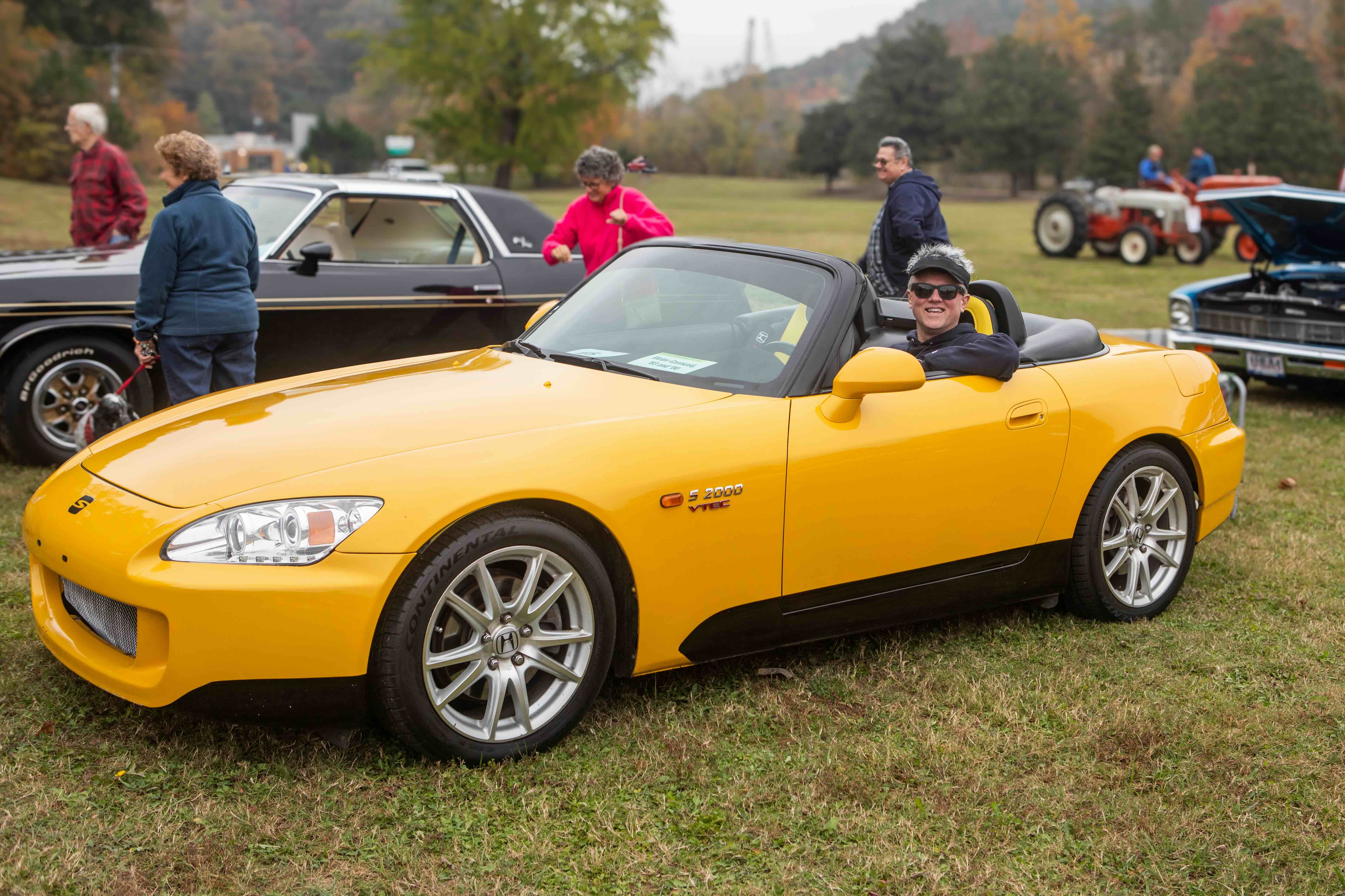 Homecoming Weekend Photo of a man in a yellow sports car parked in the grass around other cars