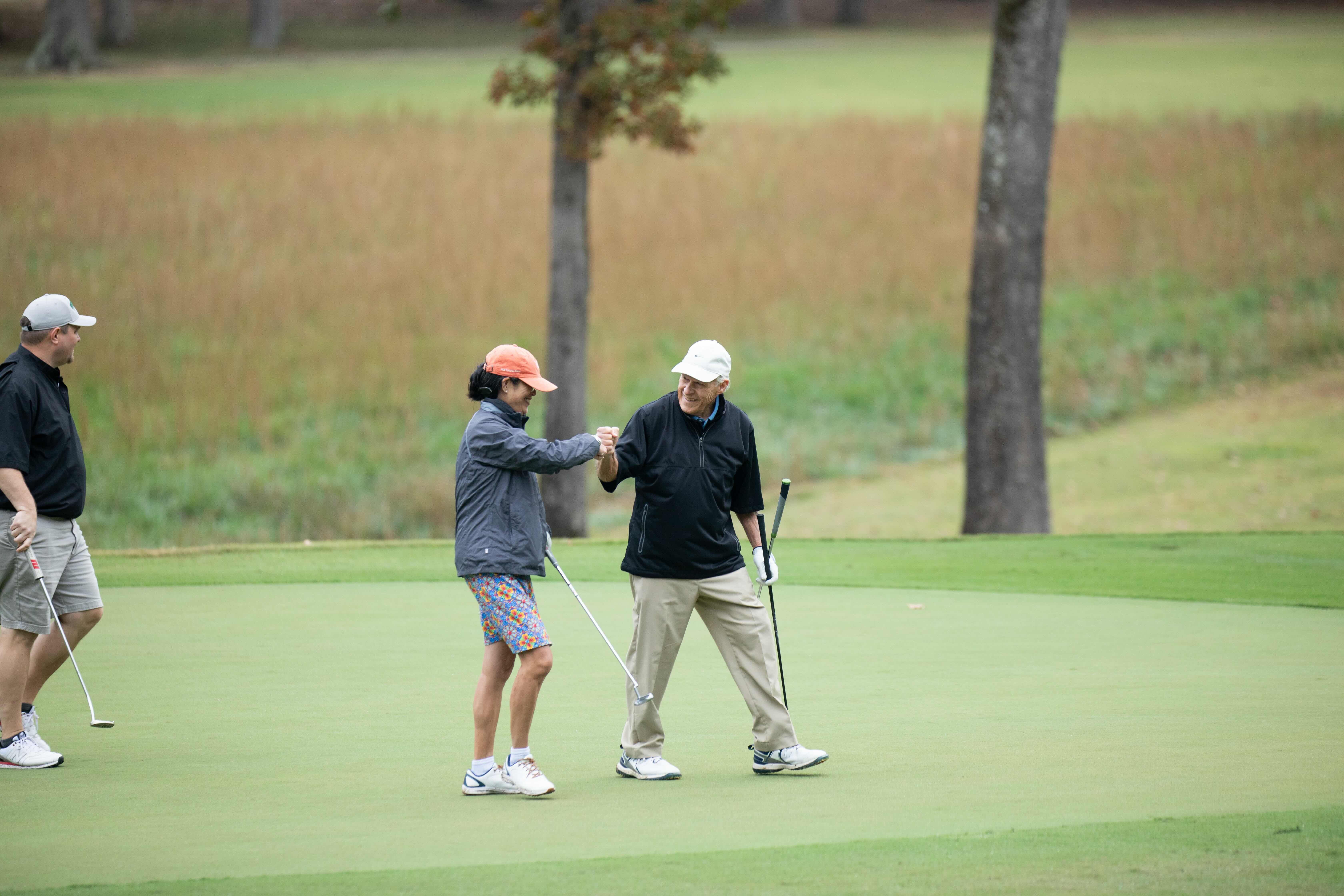 Homecoming Weekend Photo of two golfers fist bumping on the green of the course