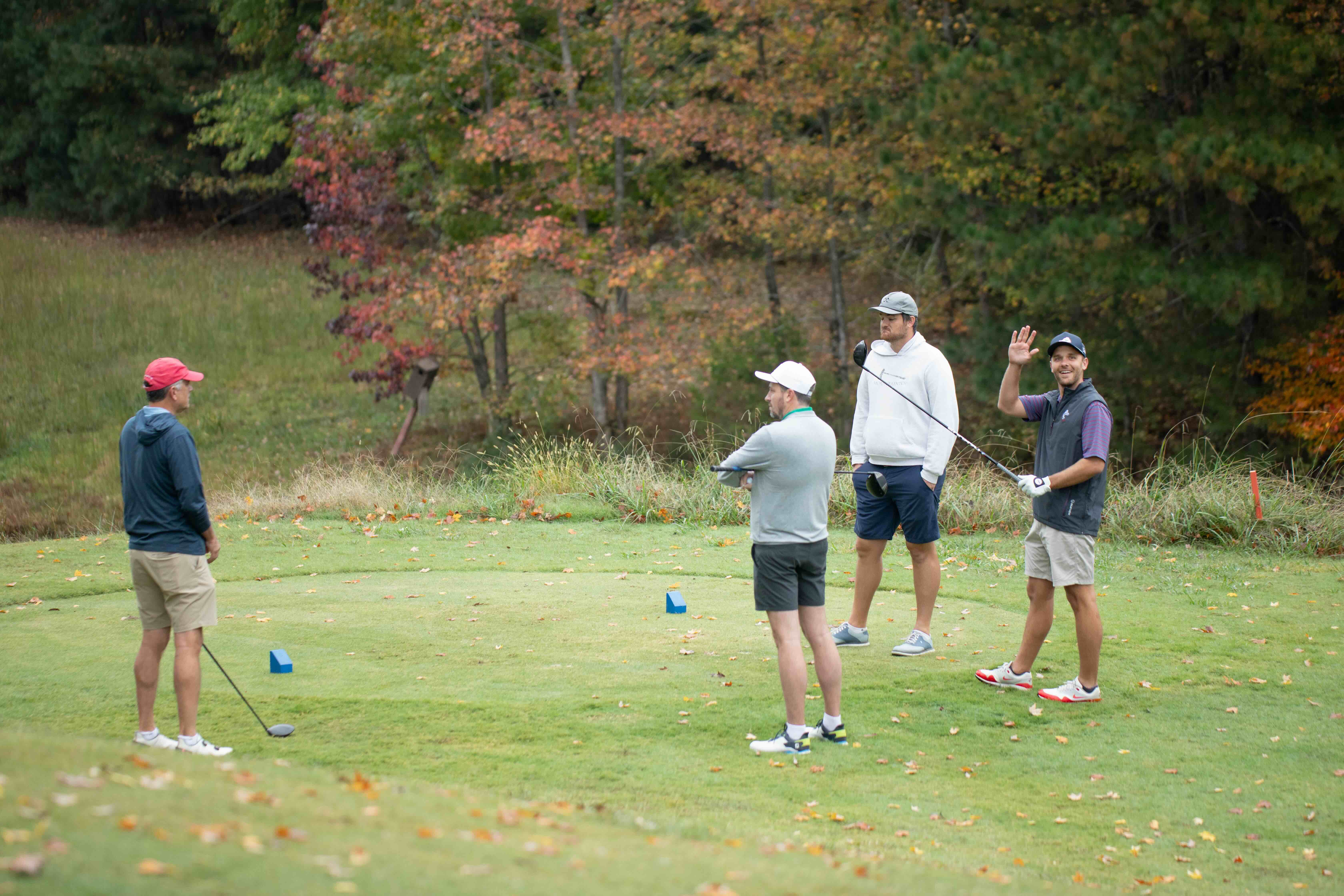 Homecoming Weekend Photo a golf foursome preparing to tee off with one golfer waiving at the camera