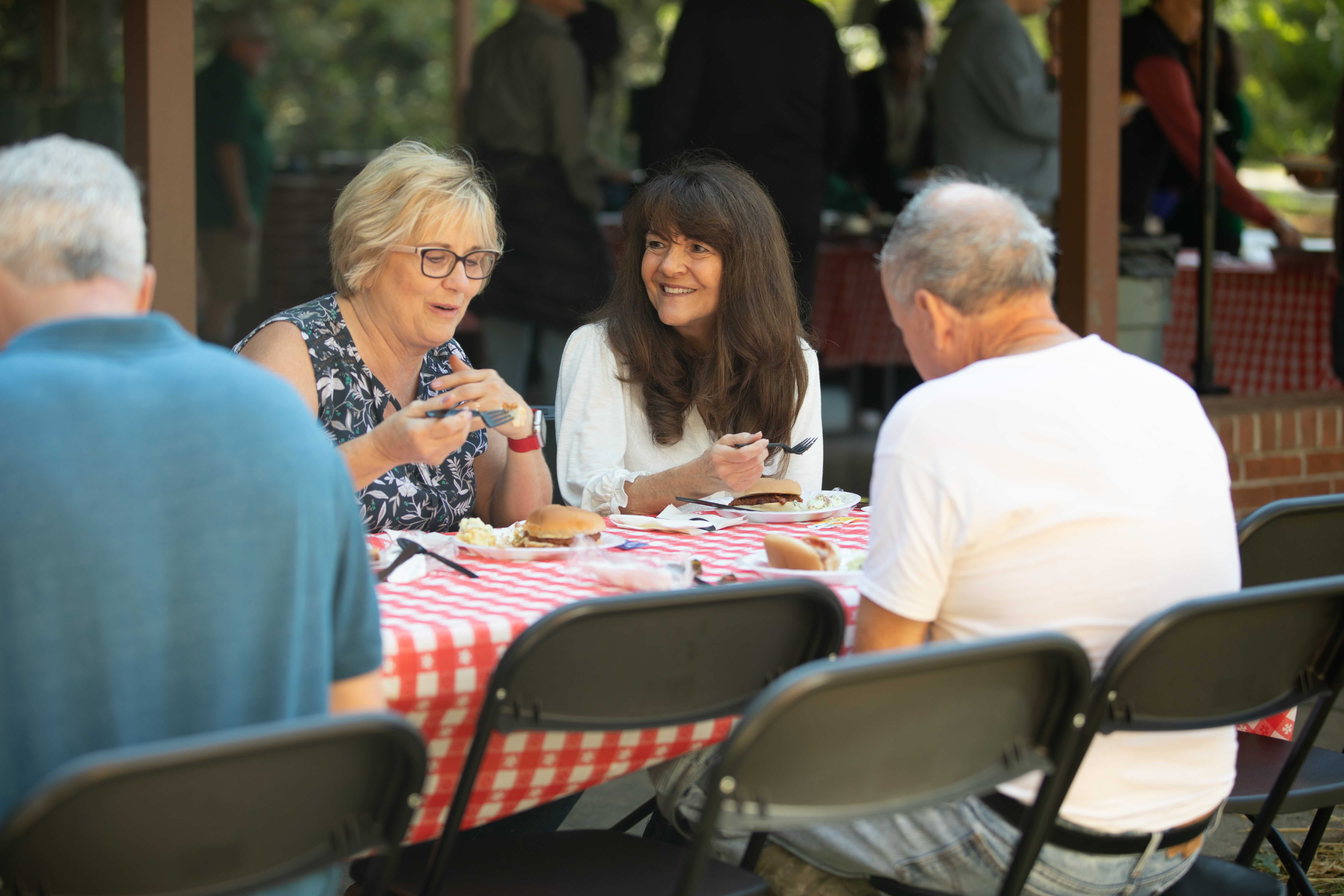 Homecoming Weekend Photo of 4 alumni eating lunch together at a picnic table