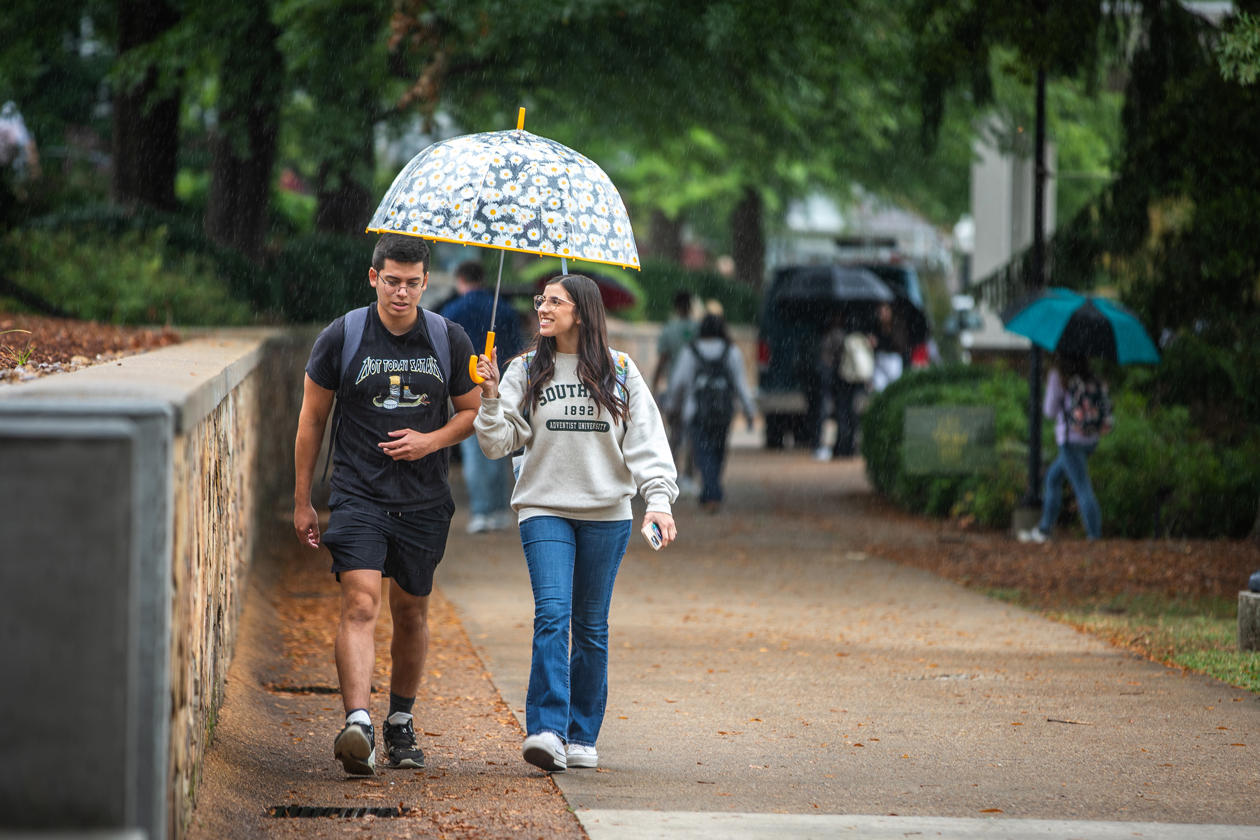 Two students walk together while one holds an umbrella over the other